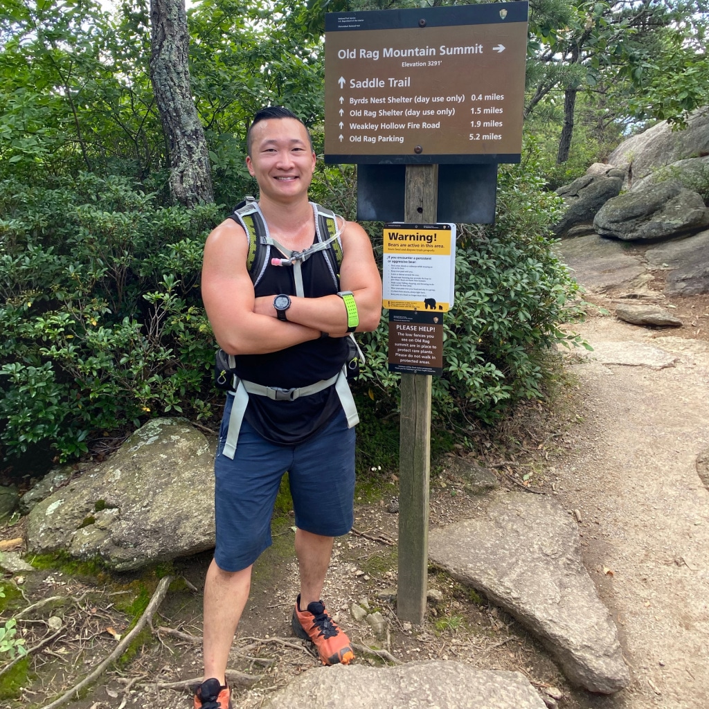 Andrew on a rocky hiking trail next to a trail marker